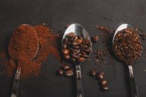 Tipos de grãos de café instantâneo e pó e café em colheres na mesa preta — Fotografia de Stock
