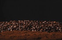 Falling fresh roasted coffee beans and powder coffee isolated on black background — Stock Photo