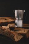 Taza de bebida de café con hervidor de agua y granos de café sobre leña aislada sobre fondo negro - foto de stock