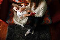 De cima de mãe satisfeita tocando bebê brincando com bebê recém-nascido animado com boca aberta se divertindo deitado na cama em casa — Fotografia de Stock