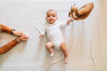 Top view of curious newborn infant with open mouth in white pajama playing with dog lying on bed looking at camera — Stock Photo