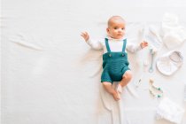 Вид изумленного новорожденного в повседневной одежде, лежащего на кровати рядом с игрушками, глядя в камеру — стоковое фото