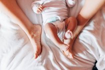 Top view of crop newborn baby in diaper lying on bed with mother in house — Stock Photo