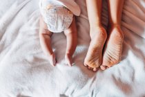 Top view of crop newborn baby in diaper lying on bed with mother in house — Stock Photo