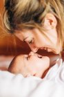 Крупним планом щаслива мама торкається носа носом дитини, грає з новонародженим немовлям з відкритим ротом розважається лежачи на ліжку вдома — стокове фото
