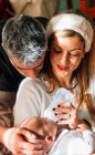 Madre satisfecha alimentando al recién nacido con biberón de leche y padre cariñoso acariciando la cabeza del bebé en casa - foto de stock