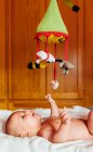 Side view of cheerful naked baby with open mouth playing with toy lying on bed having fun at home — Stock Photo