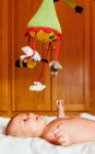 Side view of cheerful naked baby with open mouth playing with toy lying on bed having fun at home — Stock Photo