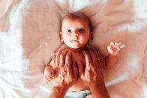 Top view of crop father touching peaceful infant lying on bed at home looking at camera — Stock Photo