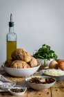 Ciotole con fronzoli patate ripiene erbe verdi funghi fritti uova formaggio grattugiato e bottiglia con olio d'oliva sul tavolo di legno — Foto stock