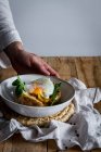 Урожай анонімної руки тримає тарілку зі смаженим яйцем на картоплі на дерев'яному столі зі смаженими грибами тертим сиром і травами — стокове фото