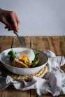 Crop anonymous hand holding dish with fried egg on potato on wooden table with fried mushrooms grated cheese and herbs — Stock Photo