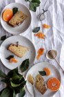 De cima bolo doce apetitoso e mandarina de laranja madura cortada e servida em pratos brancos na mesa decorada com plantas — Fotografia de Stock