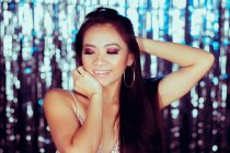 Glamour lungo dai capelli asiatico donna alzando mano e guardando giù con sorriso su sfondo di frizzante muro — Foto stock