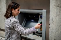 Vista lateral da senhora de cabelos pretos bem vestida inserindo cartão de crédito para ATM — Fotografia de Stock