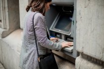 Seitenansicht einer gut gekleideten schwarzhaarigen Dame, die Kreditkarte in den Geldautomaten eingibt — Stockfoto