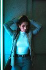 Adolescente donna in jeans casual e giacca grigia in piedi e testa tremante con capelli neri ondulanti in luce al neon — Foto stock