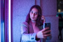 Женщина фотографирует на мобильные телефоны, держась за руки перед камерой в неоновом свете — стоковое фото