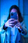 Unrecognizable female hipster taking picture on mobile phones holding in hands in front of camera in neon light — Stock Photo