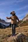 Ragazzo intelligente attivo che distoglie lo sguardo in occhiali VR in piedi sulla pietra nella valle di montagna — Foto stock