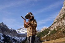 Активный умный мальчик смотрит в очки виртуальной реальности, играя с палкой, стоящей на камне в горной долине — стоковое фото
