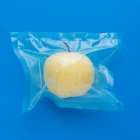 Вид зверху на стигле жовте очищене яблуко у вакуумній пластиковій сумці на синьому фоні — стокове фото
