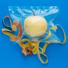 Vista dall'alto di mela sbucciata gialla matura in sacchetto di plastica sottovuoto e buccia di mela su sfondo blu — Foto stock