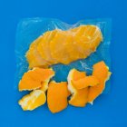 Vista superior de naranja pelada madura en bolsa de plástico al vacío y cáscara de naranja sobre fondo azul - foto de stock
