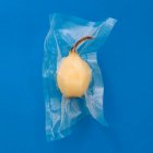 Visão superior da pêra descascada amarela madura no saco de plástico a vácuo no fundo azul — Fotografia de Stock