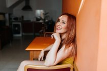 Vista lateral de cima de ruiva conteúdo mulher rindo e olhando para longe enquanto descansa na cadeira na cozinha moderna — Fotografia de Stock