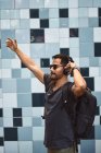 Glücklicher hispanischer Mann in Freizeitkleidung und Rucksack mit Kopfhörern, der an der Straße steht und Musik hört — Stockfoto