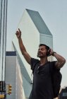 Glücklicher hispanischer Mann mit geschlossenen Augen in Freizeitkleidung und Rucksack mit Kopfhörern, der an der Stadtstraße Musik hört — Stockfoto
