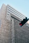 Dal basso del semaforo nero con il colore rosso e l'edificio moderno con architettura creativa sotto il cielo blu sullo sfondo — Foto stock