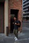 Вид збоку його іспаномовного чоловіка мандрівника в повсякденному вбранні з рюкзаком, що стоїть уздовж порожньої вулиці міста з цегляною будівлею на фоні — стокове фото