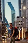 Side view of pleased Hispanic male traveler with backpack in casual outfit laughing while strolling at modern downtown — Stock Photo