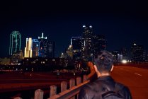 Vista posteriore dell'uomo anonimo in giacca di pelle nera casual con zaino che cammina di notte città su sfondo sfocato — Foto stock