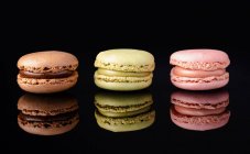 Colorful tasty macaroons stacked displayed on black background — Stock Photo