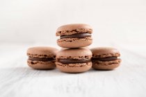 Brown tasty macaroons stacked in pile against wooden white surface — Stock Photo