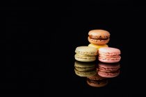 Colorful tasty macaroons stacked displayed on black background — Stock Photo
