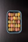 Macaroons saborosos coloridos exibidos dentro do recipiente azul no fundo preto — Fotografia de Stock