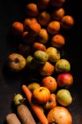 Зверху свіжі соковиті яблука мандарин з гранатом і апельсиновою морквою на чорній поверхні у світлі — стокове фото
