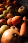 Сверху свежие сочные яблоки мандарин с гранатом и оранжевой морковью на черной поверхности при свете — стоковое фото