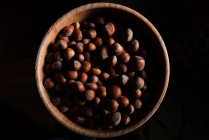 Dall'alto ciotola di legno marrone pieno di gustosa nocciola fresca su sfondo nero — Foto stock