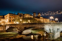 Величественный пейзаж древнего освещенного моста над рекой, отражающего городской свет в Жироне, Каталония, Испания — стоковое фото