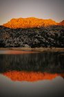 Paisagem colorida brilhante de topo laranja e montanha cinza coberta com árvores cercadas por águas claras refletindo rochas — Fotografia de Stock