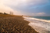 Paisagem pacífica da cidade vazia à beira-mar e ondas espumosas turquesa sob céu nublado em dia brilhante — Fotografia de Stock