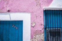 Shabby wall colored in pink and wooden door with number 200 and window in bright day — Stock Photo