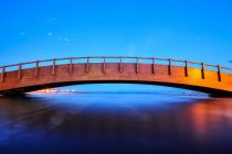 Einwandfreie Landschaft der antiken Konstruktion einer Holzbrücke über klares Wasser, das den blauen Himmel im Abendlicht reflektiert — Stockfoto