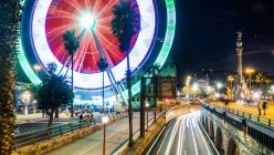 Paisagem colorida de vista noturna da cidade com estrada e roda gigante iluminada e rua decorada com palmeiras — Fotografia de Stock