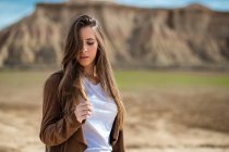 Riflessivo viaggiatore donna seducente con gli occhi chiusi in piedi vicino a grande montagna e cielo blu sullo sfondo in Bardenas Reales, Navarra, Spagna — Foto stock